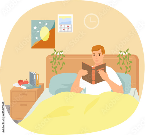 Cute man in pajamas reading literature on his bed comfortably. Book lover concept with young man lying relax on sofa and reading book. Concept of homeward and comfort. Person relaxes after work