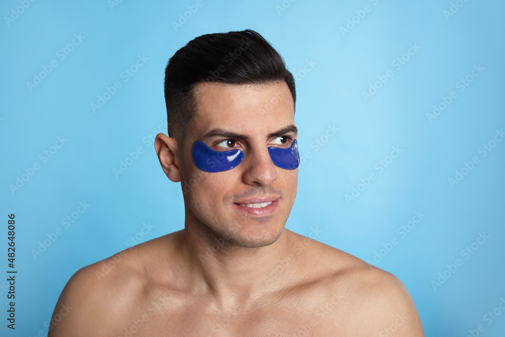 Man with under eye patches on light blue background Man with under eye patches on light blue background