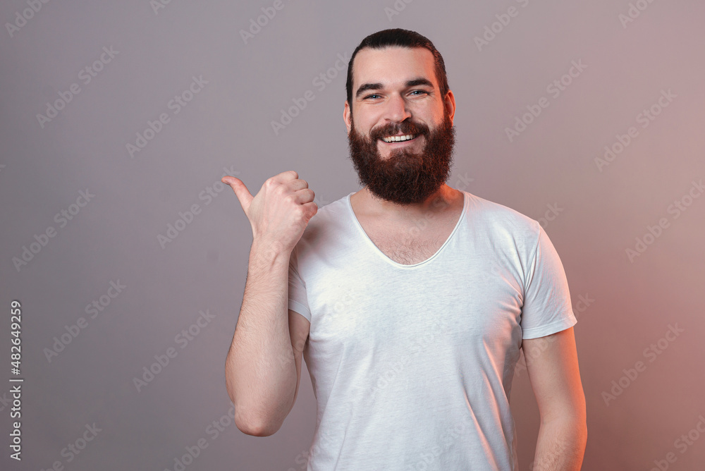 Photo of young bearded hipster man pointing at the corning and smiling at the camera. Photo of young bearded hipster man pointing at the corning and smiling at the camera.