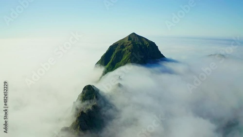 Aerial serene panorama. High green peak above endless dense white clouds around