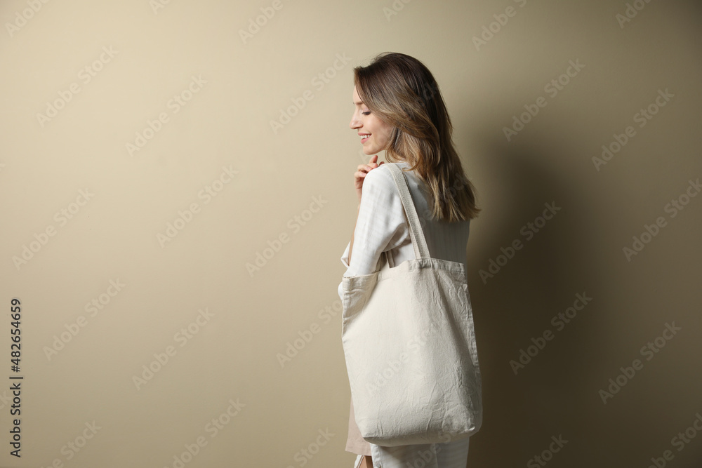 Happy young woman with blank eco friendly bag against beige background. Space for text Happy young woman with blank eco friendly bag against beige background. Space for text