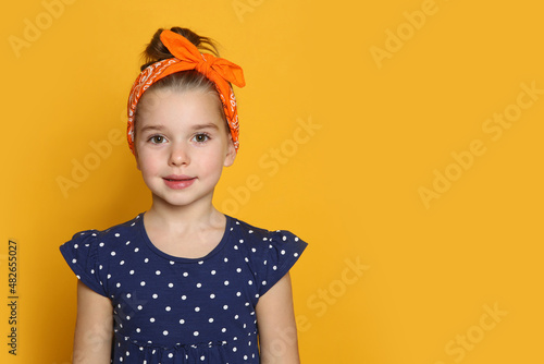 Cute little girl wearing stylish bandana on orange background, space for text photo