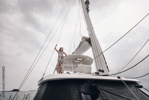Perfect fit girl in a colorful dress is posing on a snow-white yacht, wide angle