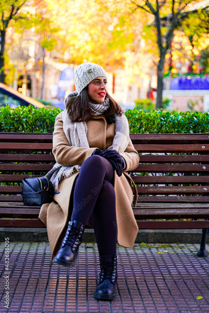 Elegant adult woman smiling and pensive, sitting on a wooden bench Elegant adult woman smiling and pensive, sitting on a wooden bench
