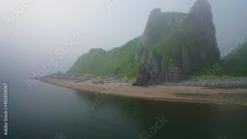 Misty panorama. Flying above calm blue sea to green hills at deserted sand beach
