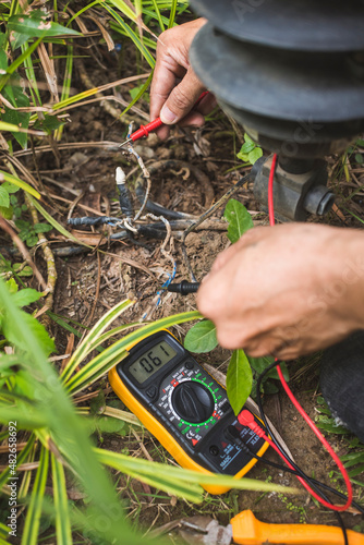 An electrician tests an exposed grounded wire with a digital multimeter with LCD screen. Safety procedure at a home garden. photo