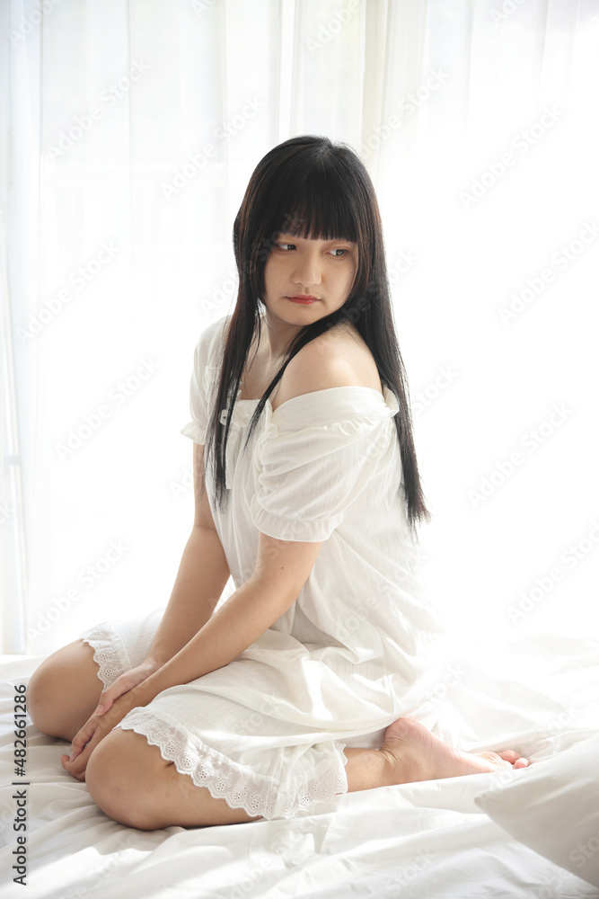 Beautiful young Asian sitting on bed relaxing in the morning light with white room Beautiful young Asian sitting on bed relaxing in the morning light with white room