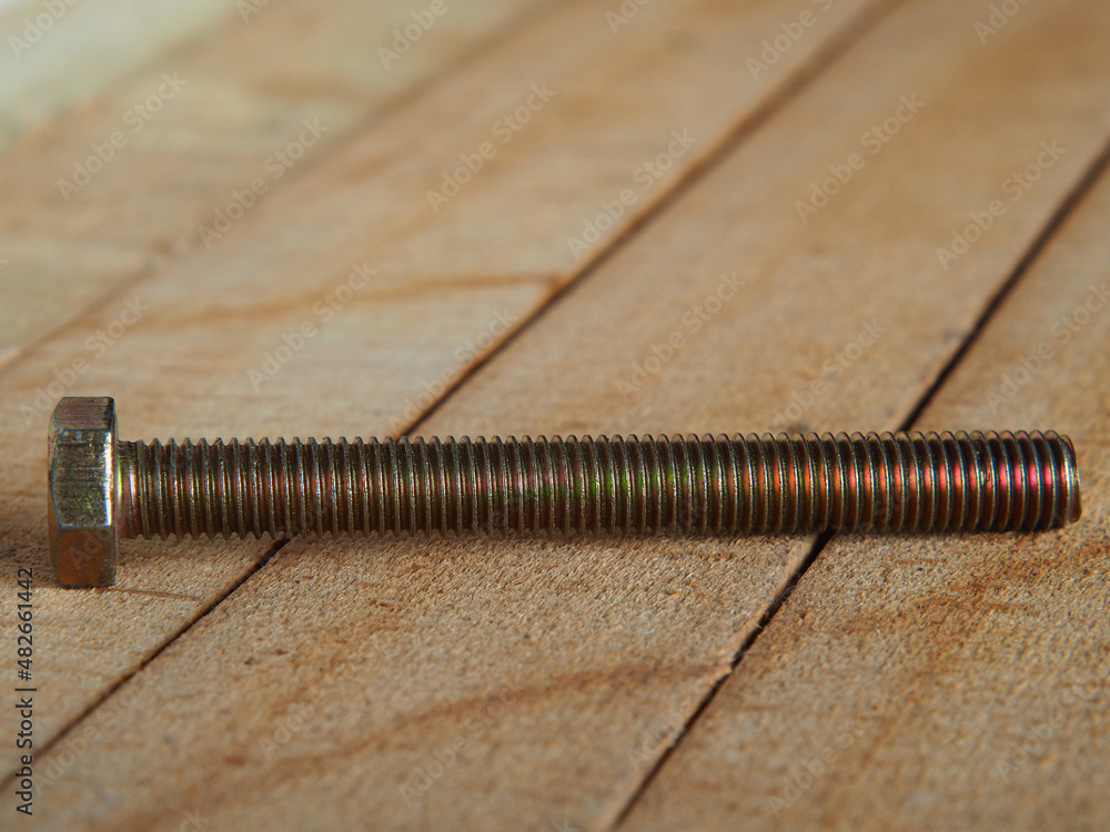Golden bolt. Chromeplated metal bolt on wooden planks, shallow depth