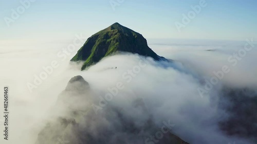 Aerial tranquil panorama. High green peak above dense white clouds flow around