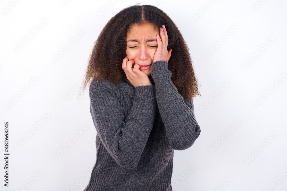 Doleful desperate crying teenager girl wearing grey sweater standing against wite background , looks stressfully, frowns face, feels lonely and anxious Doleful desperate crying teenager girl wearing grey sweater standing against wite background , looks stressfully, frowns face, feels lonely and anxious