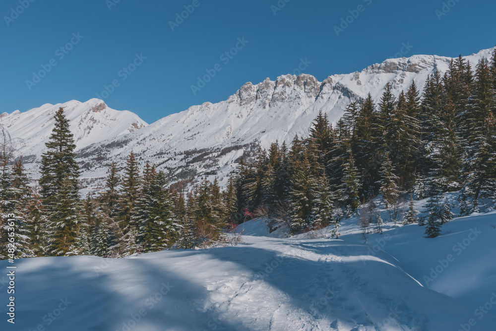 A picturesque landscape view of the snowcapped French Alps mountains with a hiking path in the snow on a cold winter day (Devoluy)