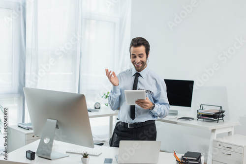 cheerful security man gesturing while looking at digital tablet in surveillance room. © LIGHTFIELD STUDIOS