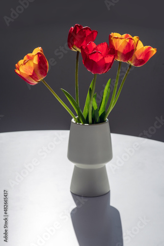 Bouquet of red and yellow tulips in a white vase on a grey background.