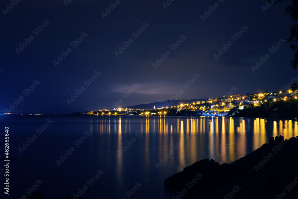 Obraz premium The lights of Novi Vinodolski town are reflected in the coastal waters of Adriatic sea in Croatia