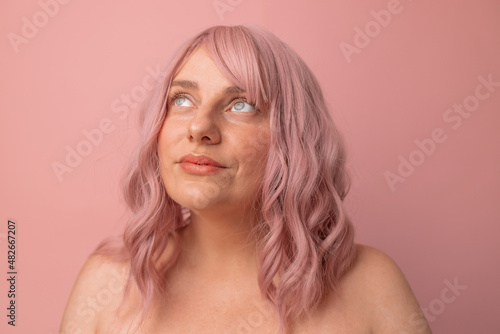 Portrait of pretty sexy girl with pink curly hair in lingerie posing isolated on pink background