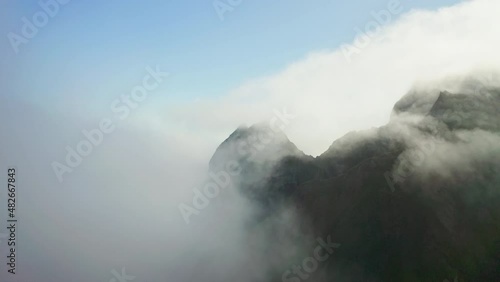 Flying over white clouds above hills at sea shoreline reveals an isle at horizon