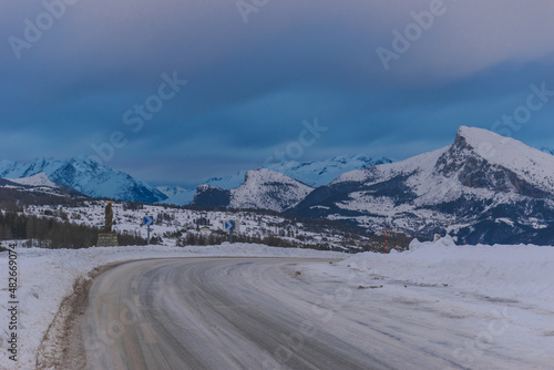 A picturesque landscape view of the road in the snowcapped French Alps mountains during the sunset on a cold winter day (Hautes-Alpes, Devoluy)