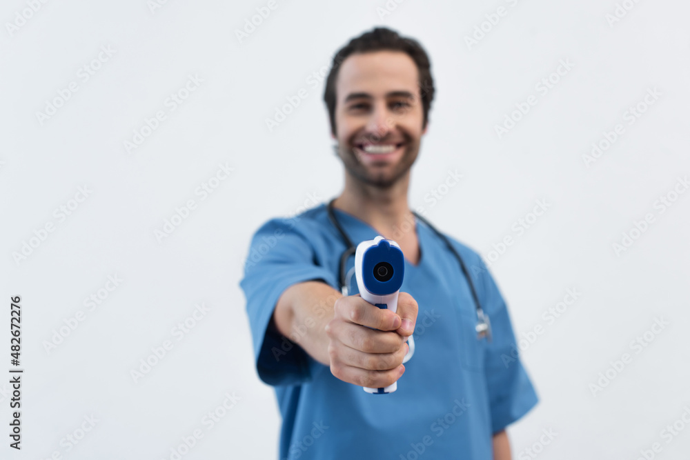 blurred doctor smiling while holding pyrometer isolated on grey. blurred doctor smiling while holding pyrometer isolated on grey.