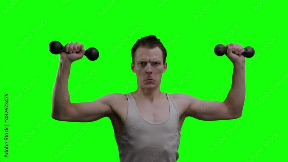 A young thin man in a gray T-shirt and with brown hair squats and lifts dumbbells up against a green background. Sport and healthy lifestyle concept. A young thin man in a gray T-shirt and with brown hair squats and lifts dumbbells up against a green background. Sport and healthy lifestyle concept.