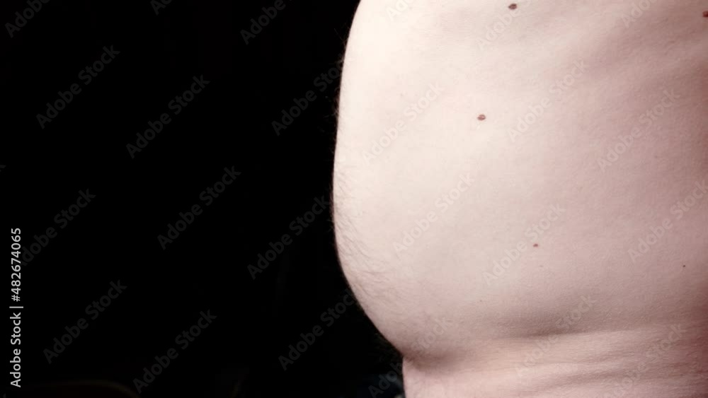 The man's fat belly increases against a dark background. Obesity, weight problems. Time for diet, sports concept. The man's fat belly increases against a dark background. Obesity, weight problems. Time for diet, sports concept.
