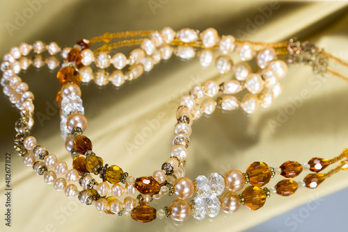 Selective focus photo of pretty vintage necklaces with crystal beads and baroque pearls on reflective surface