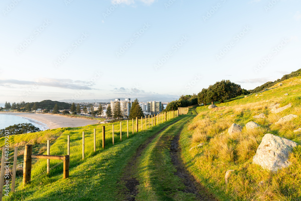 Track around Mount Maunganui along fence-line with view out to buildings in town and ocean beach.