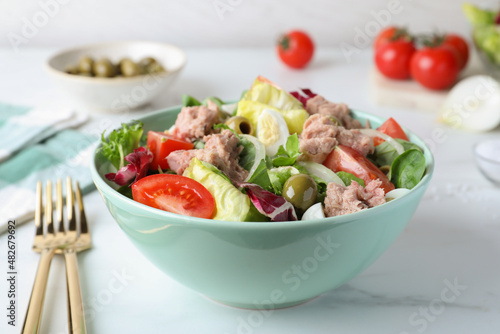 Bowl of delicious salad with canned tuna and vegetables served on white marble table