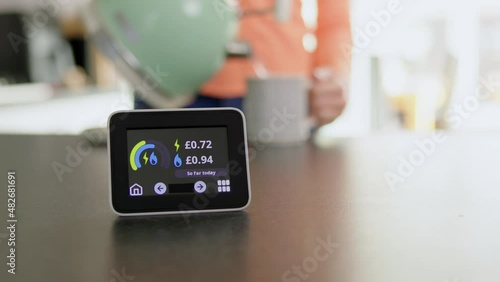 Close Up Of Smart Energy Meter In Kitchen Measuring Electricity And Gas Use With Woman Boiling Kettle