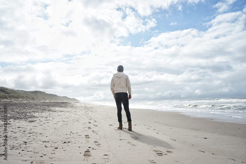 Person standing on a sunny beach in winter Person standing on a sunny beach in winter