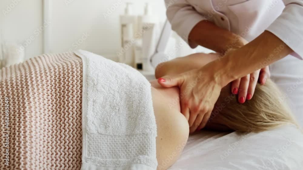 Relaxed woman receiving neck cervical spine massage in aesthetic salon. Getting procedure in beauty clinic. Stress relief and rejuvenation concept. Relaxed woman receiving neck cervical spine massage in aesthetic salon. Getting procedure in beauty clinic. Stress relief and rejuvenation concept.