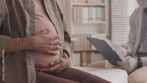 Cropped slowmo shot of unrecognizable pregnant woman stroking her belly while sitting on medical couch at doctor office