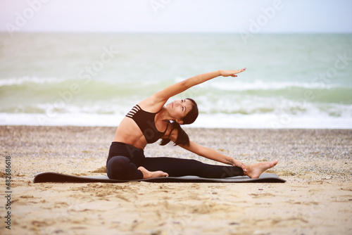 A portrait of beautiful woman stretching her arms and legs on the beach. Yoga sport. Healthy wellness lifestyle. Spiritual health. Personal fulfillment.