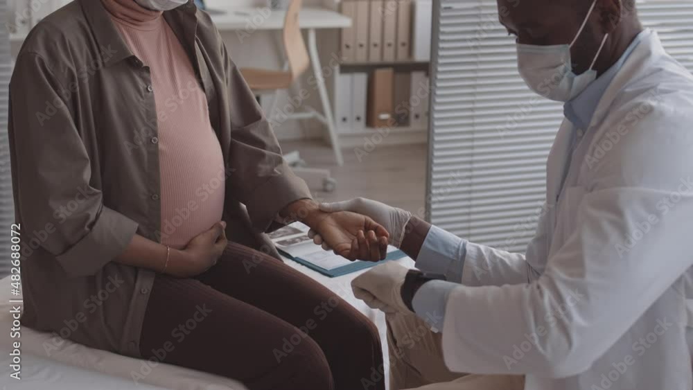 Cropped slowmo shot of African-American doctor measuring pulse of pregnant woman during appointment in modern clinic Cropped slowmo shot of African-American doctor measuring pulse of pregnant woman during appointment in modern clinic
