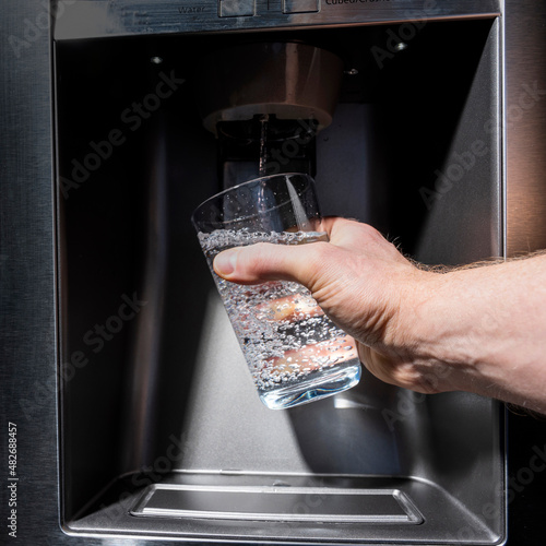 Home fridge dispenser filling glass held by male right hand point of view