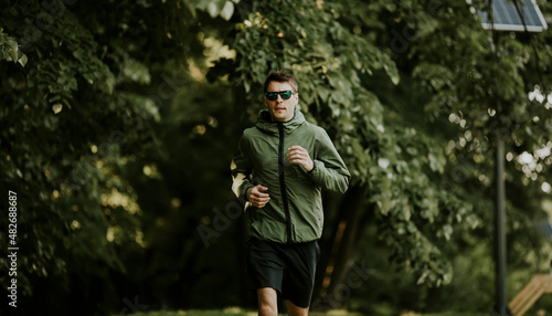 Athletic young man running while doing workout in sunny green park