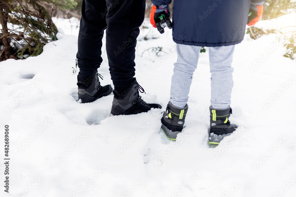 Father and son walking in winter forest, park. Two people walking on a snow covered sidewalk. Unrecognized people wearing winter boots standing on the snow during the day, outdoor. Father and son walking in winter forest, park. Two people walking on a snow covered sidewalk. Unrecognized people wearing winter boots standing on the snow during the day, outdoor.