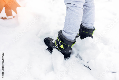 Children's winter boots in grey color on the snow. Kids winter boots walking on snowy sleet road, rear view. Close up view on shoes on snowy path, copy space.