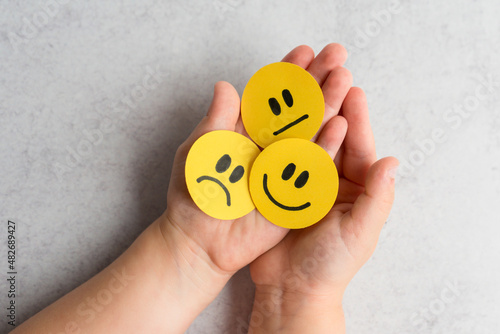 kids emotional intelligence. Little kid holding happy sad and unsatisfied yellow faces.  photo