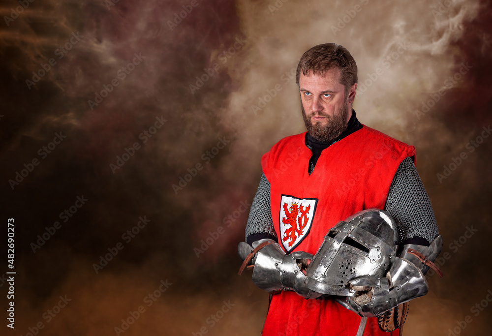 A man, a warrior, a medieval knight, dressed in armor, a cloak, with a helmet in his hands.  A brave warrior knight. Historical concept