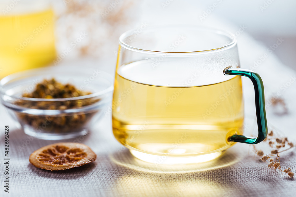 Cup of chamomile tea in transparent mug served with slice of lemon and orange. Tea break. Cup of chamomile tea in transparent mug served with slice of lemon and orange. Tea break.