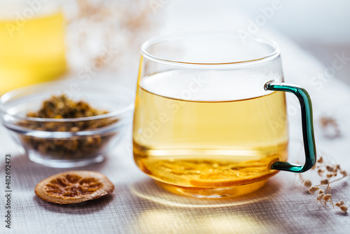 Cup of chamomile tea in transparent mug served with slice of lemon and orange. Tea break. 
