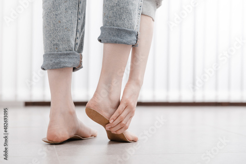 Woman fitting orthopedic insole indoors, close up. Girl holding an insole next to foot at home. Orthopedic insoles. Foot care banner. Flat Feet Correction. Treatment and prevention of foot diseases © mlphoto