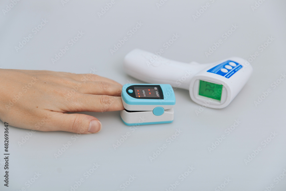 Pulse oximeter and thermometer gun on white background. Measuring oxygen saturation, pulse rate and oxygen levels. Infrared isometric thermometer gun to check body temperature for virus symptoms Pulse oximeter and thermometer gun on white background. Measuring oxygen saturation, pulse rate and oxygen levels. Infrared isometric thermometer gun to check body temperature for virus symptoms