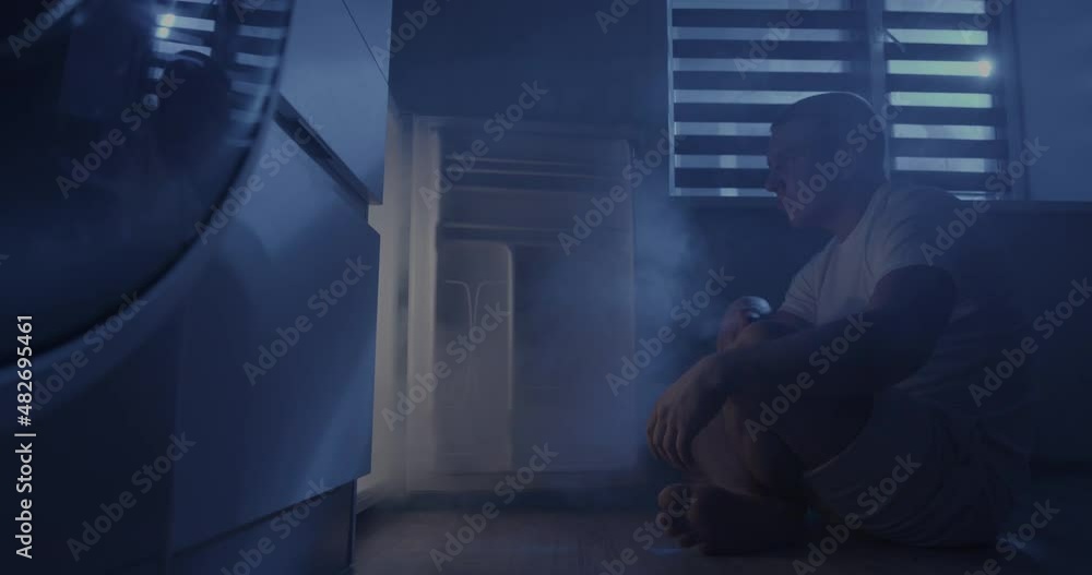 The man sits in front of the refrigerator then opens it, takes out a mug of cold beer and drinks. The man sits in front of the refrigerator then opens it, takes out a mug of cold beer and drinks.
