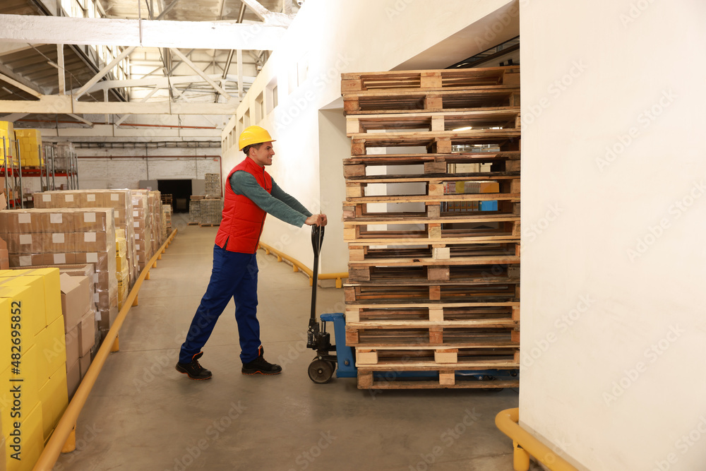 Fototapeta premium Worker moving wooden pallets with manual forklift in warehouse