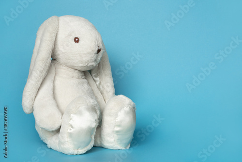 Stuffed bunny on blue background. Easter concept. Cute white toy soft bunny sitting on colored background. Copy space for text