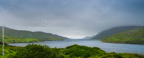 Panoramic view of a Scottish landscape with a lake, green hills and cloudy sky. © csbphoto