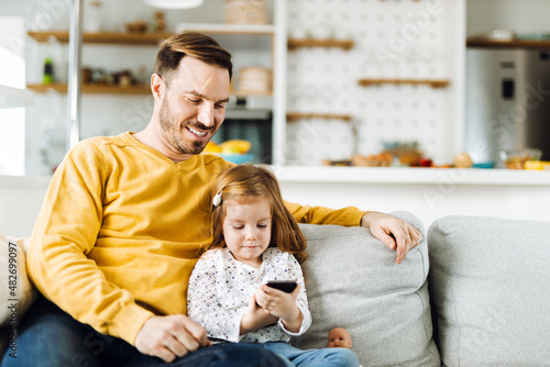 Single father and his small daughter using cell phone on sofa at home © Goran