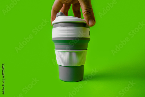 Reusable silicone cup for coffee in hand on a green background. Replacement for disposable cups.