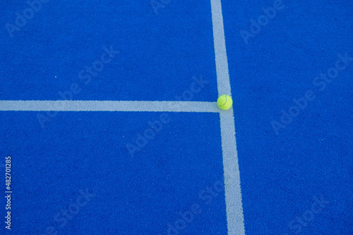 A ball on the line of a paddle tennis court of blue synthetic grass. © Vic